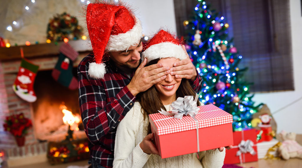 Man surprising his girlfriend with a Christmas gift in their living room de...